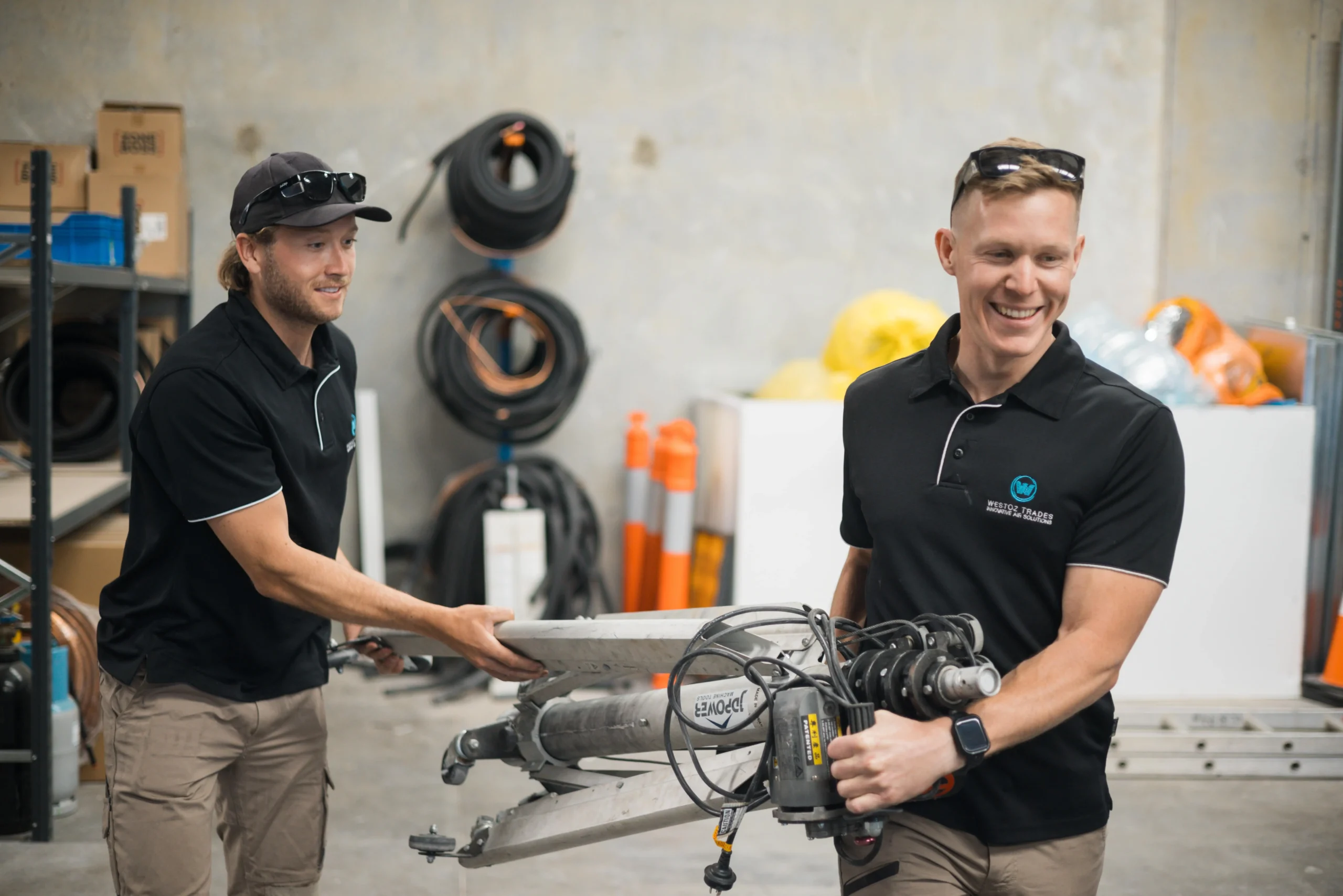 Two WestOz team members carrying equipment and working together at the warehouse, highlighting a collaborative team environment